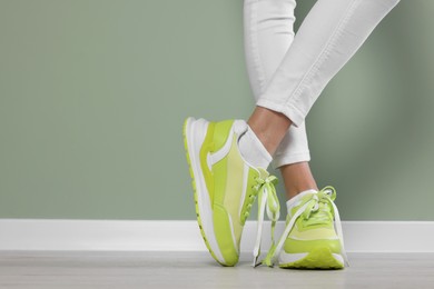 Woman wearing new stylish sneakers near light green wall, closeup. Space for text
