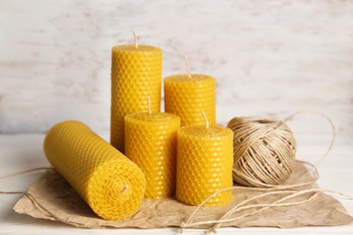 Photo of Stylish elegant beeswax candles and twine on white wooden table