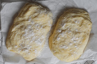 Photo of Raw dough for ciabatta and flour on parchment paper, flat lay