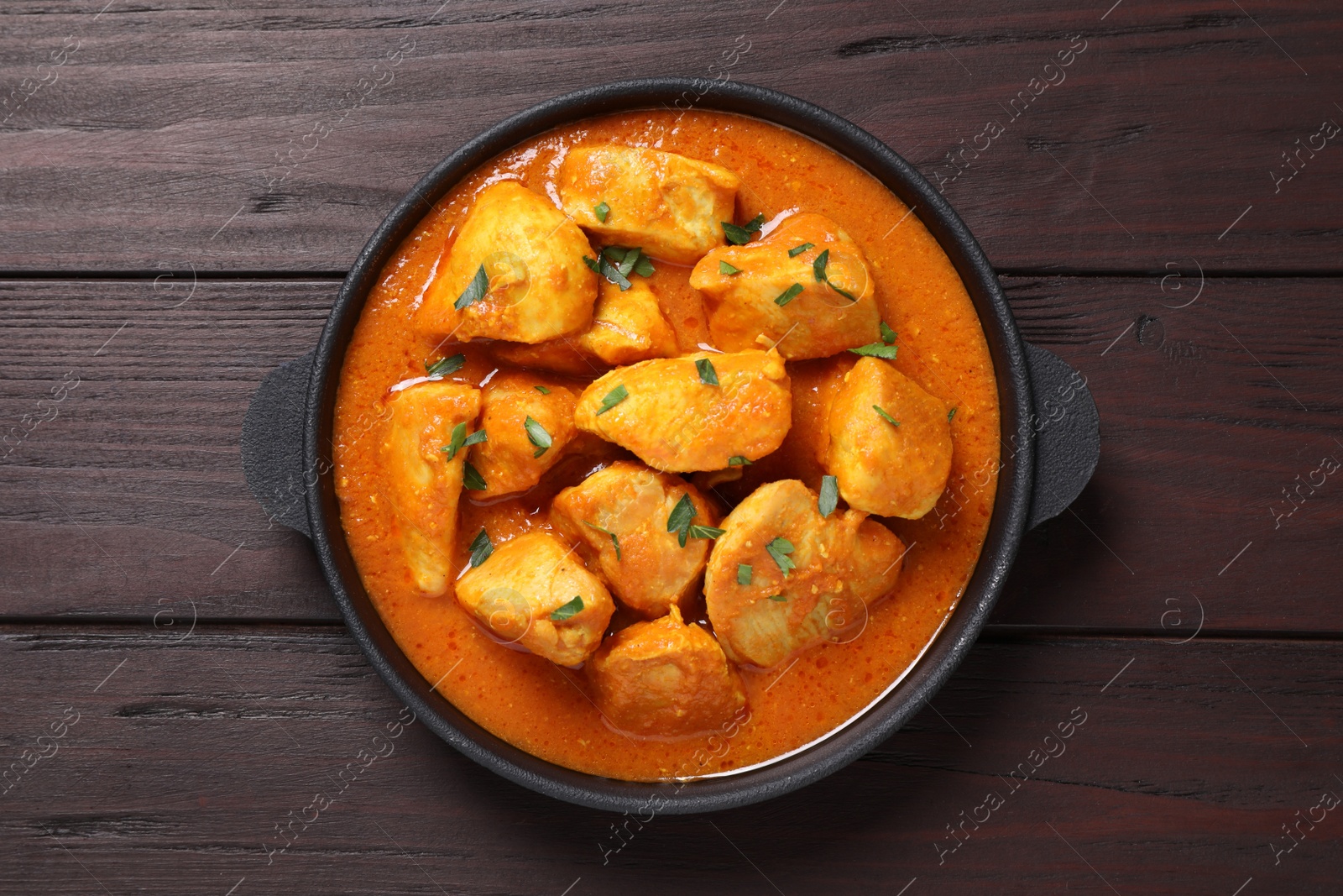 Photo of Delicious chicken curry in pan on wooden table, top view