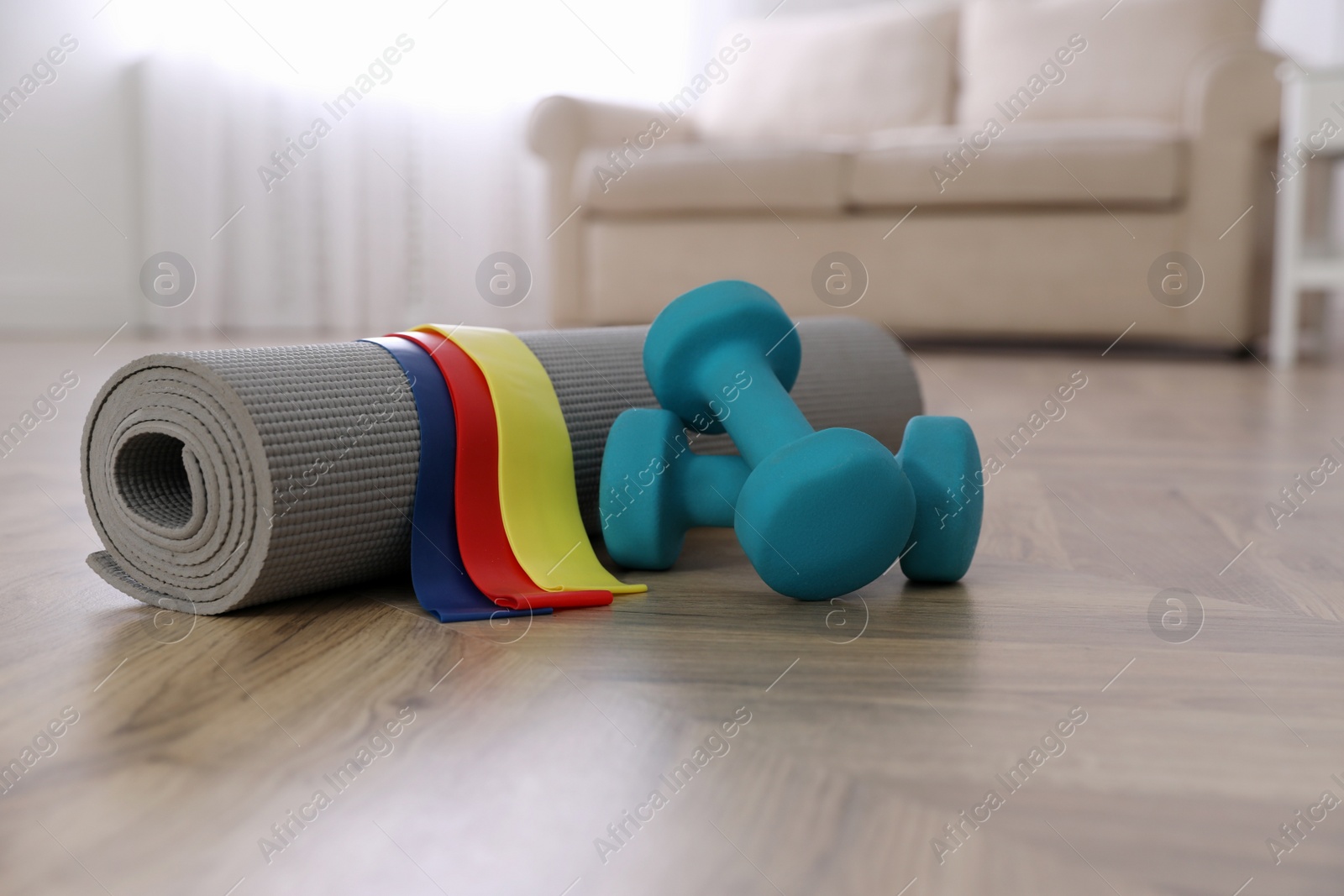 Photo of Dumbbells, elastic bands and yoga mat on floor in room, space for text. Home fitness