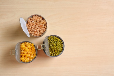 Photo of Open tin cans of conserved vegetables on wooden table, flat lay with space for text