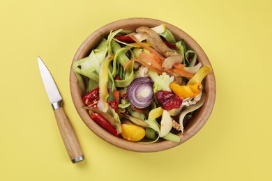 Photo of Peels of fresh vegetables and knife on yellow background, top view