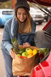 Photo of Young woman with bag of groceries near her car outdoors