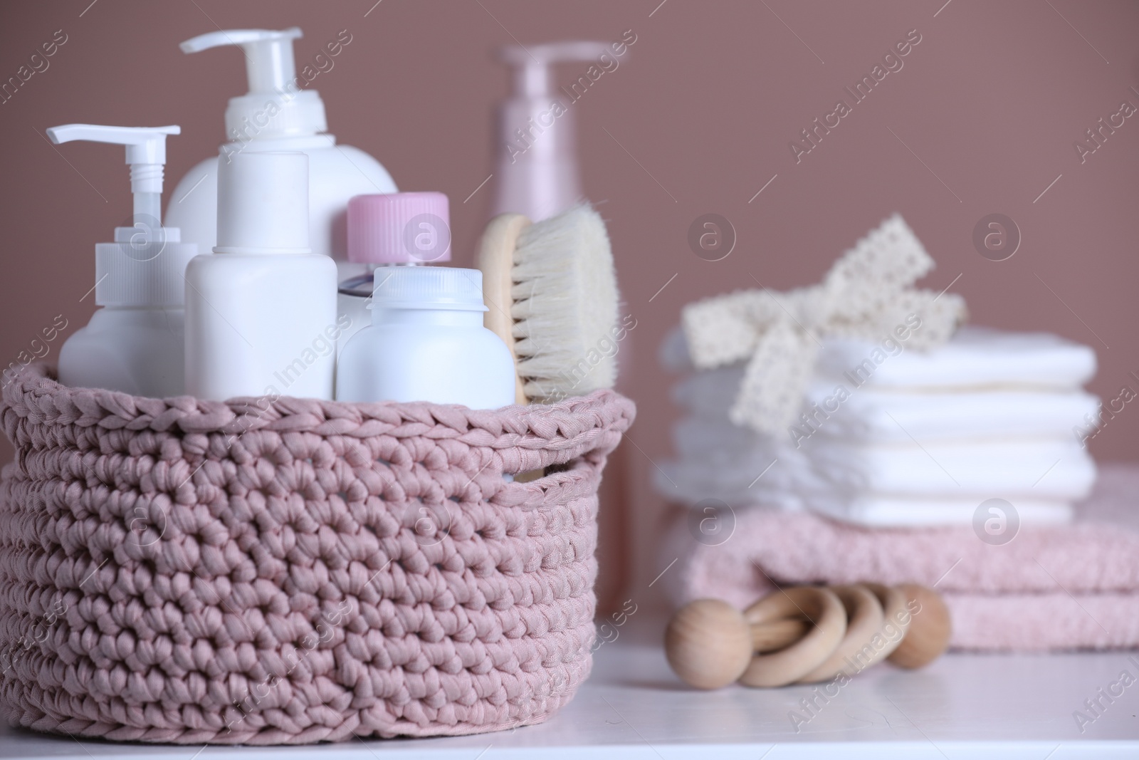 Photo of Baby cosmetic products and hair brush in knitted basket on white table. Space for text