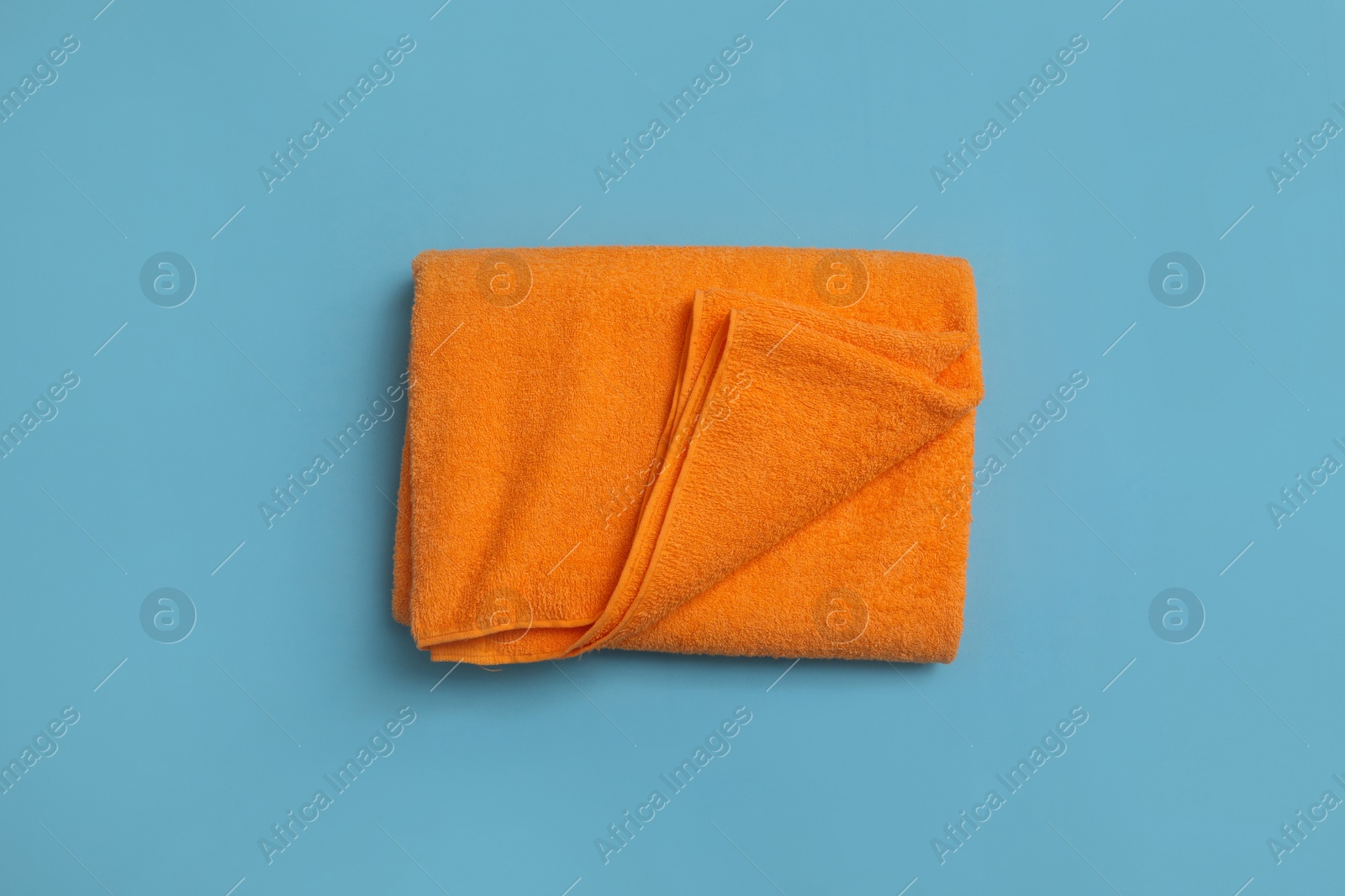 Photo of Folded orange beach towel on light blue background, top view