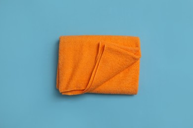 Photo of Folded orange beach towel on light blue background, top view