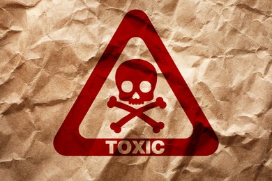 Image of Hazard warning sign (skull-and-crossbones symbol and word TOXIC) on crumpled kraft paper, top view
