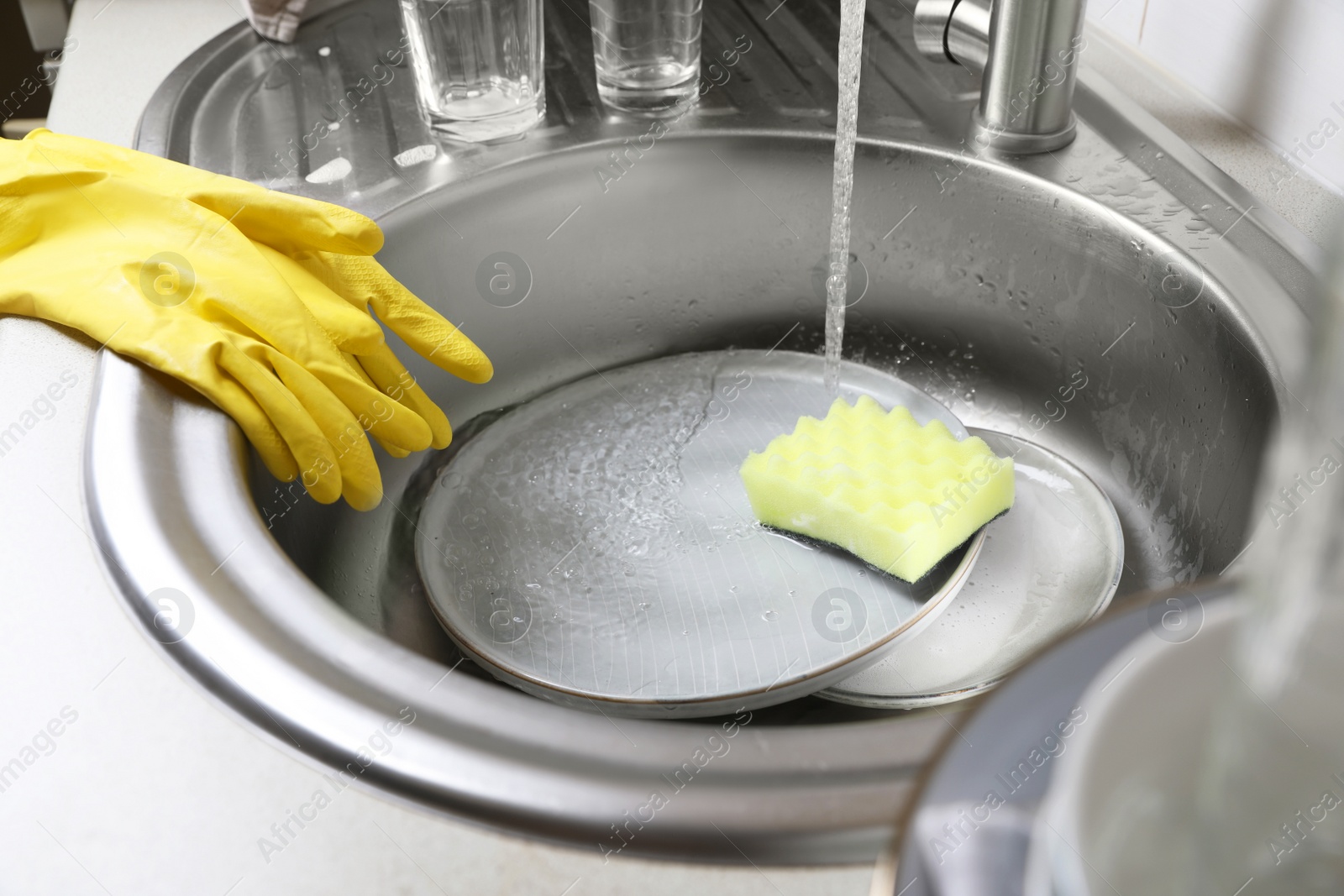 Photo of Washing plates, sponge and rubber gloves in kitchen sink