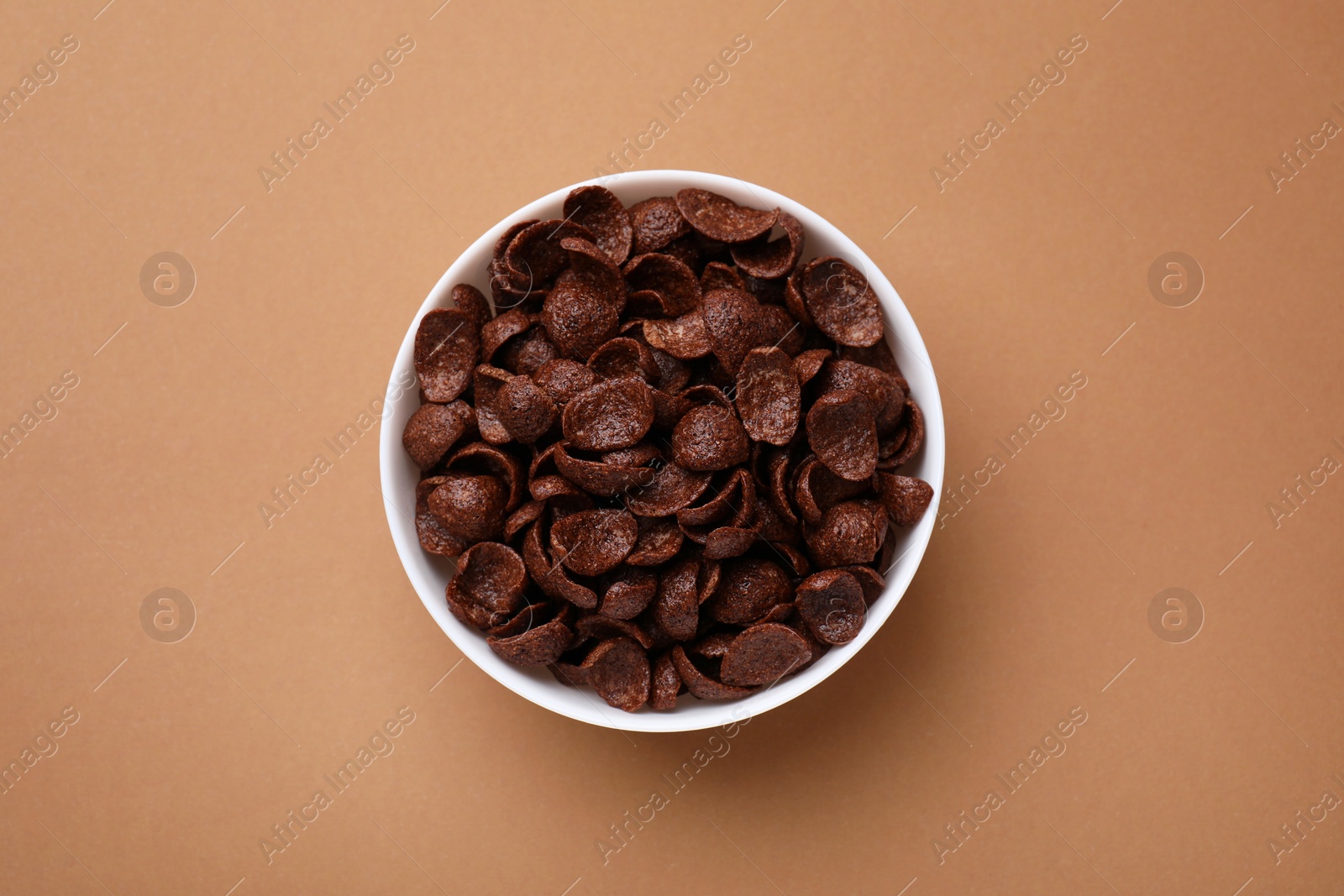 Photo of Breakfast cereal. Chocolate corn flakes in bowl on brown table, top view