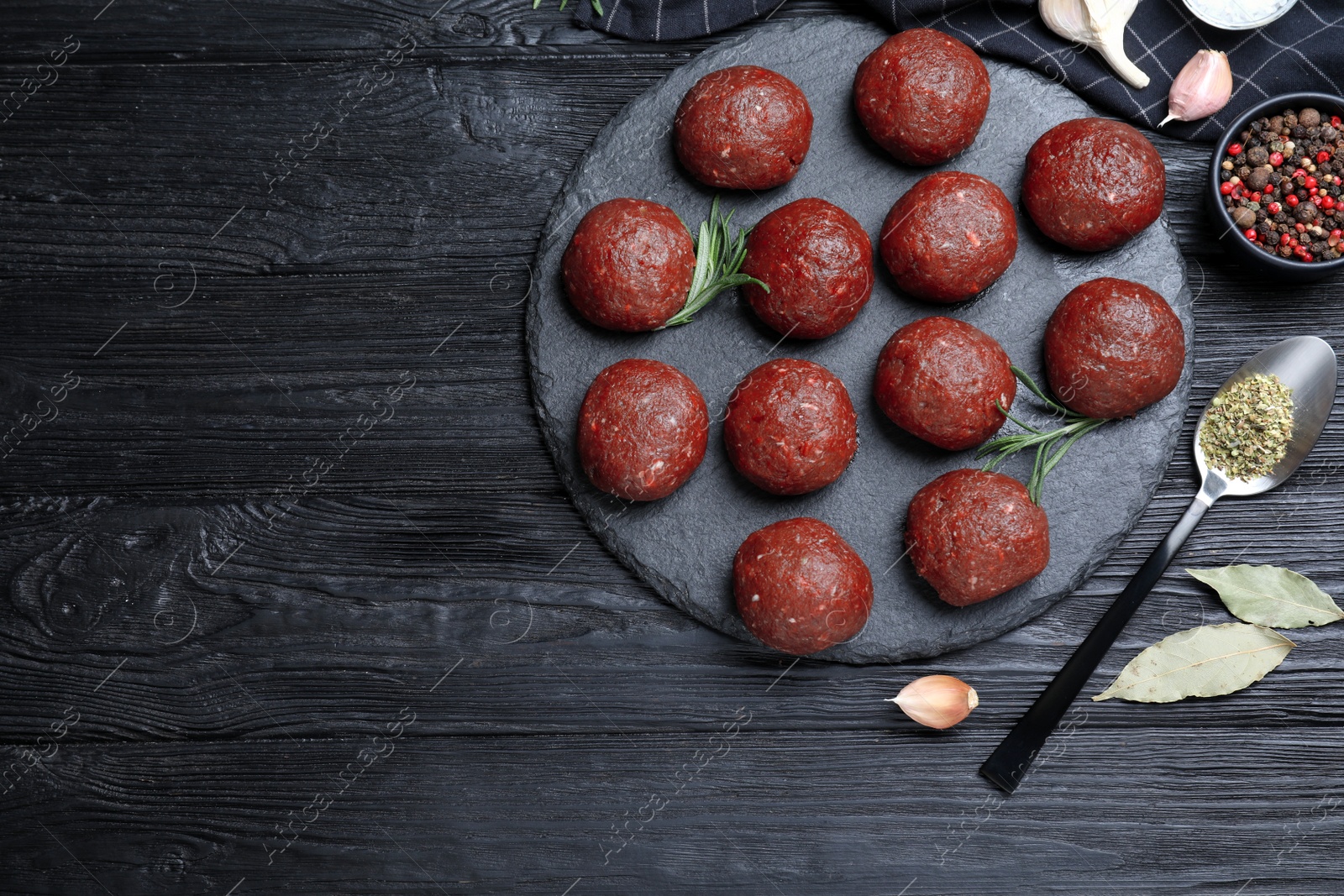 Photo of Many fresh raw meatballs on black wooden table, flat lay. Space for text