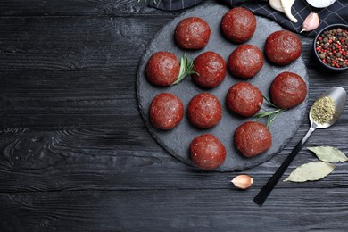 Photo of Many fresh raw meatballs on black wooden table, flat lay. Space for text