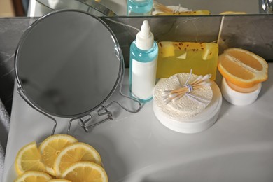 Photo of Lemon face cleanser. Fresh citrus fruits, personal care products and mirror on sink in bathroom