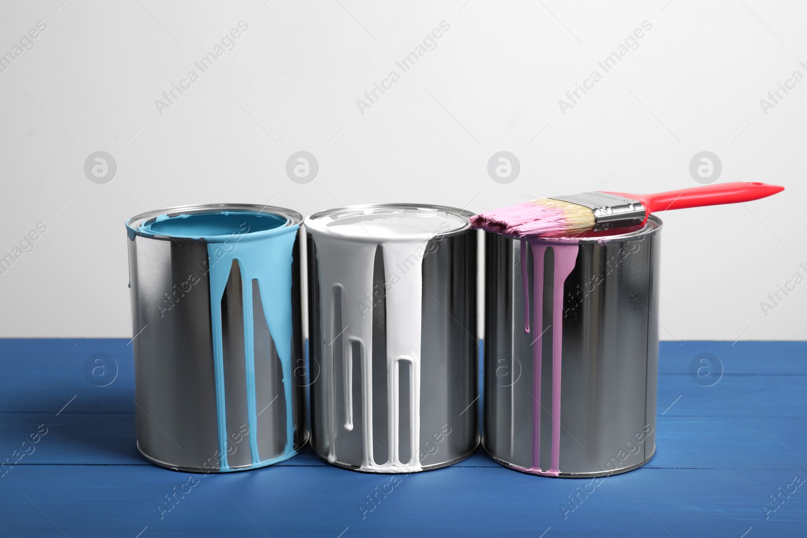 Photo of Cans of paints and brush on blue wooden table