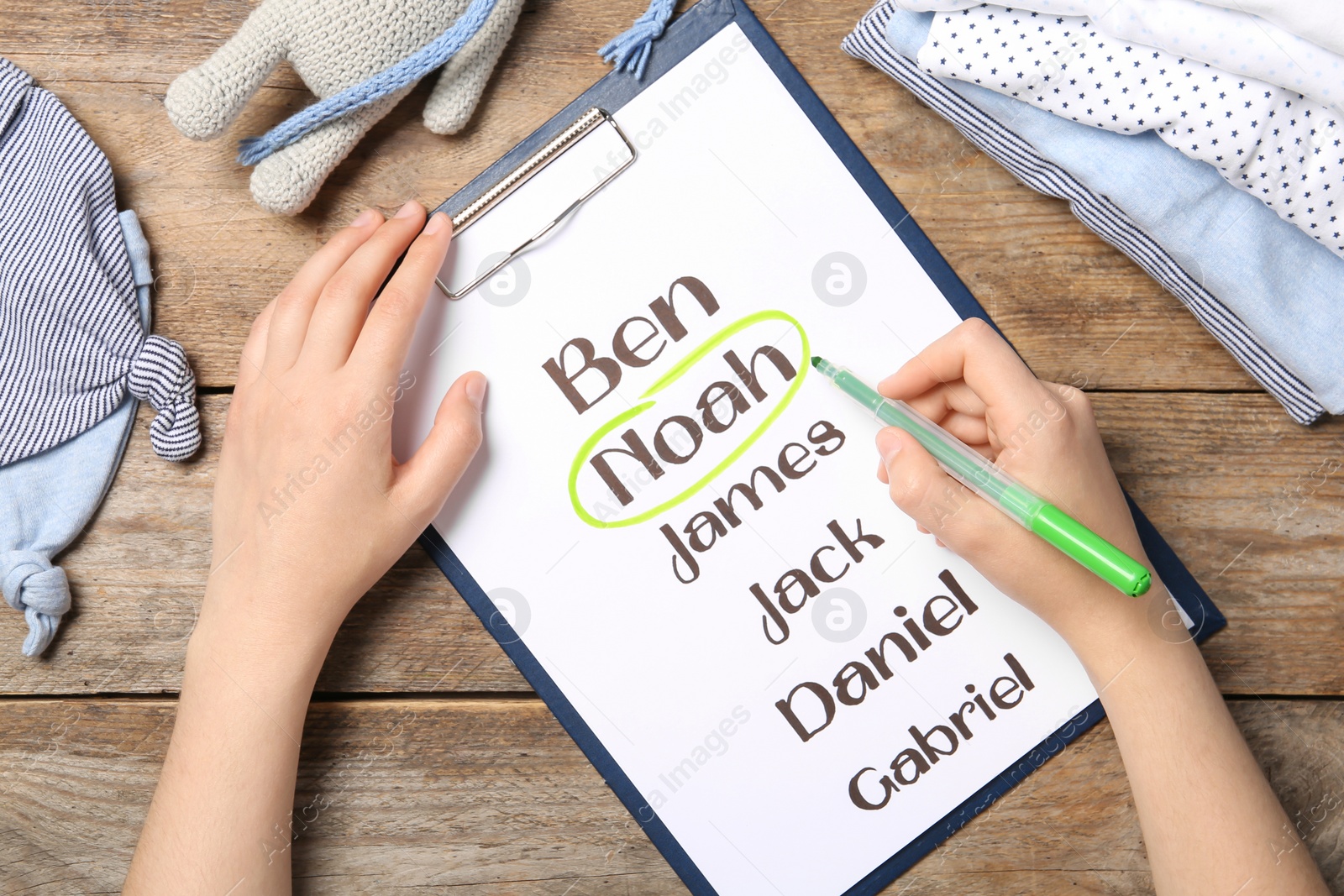 Photo of Woman marking baby name at wooden table, top view