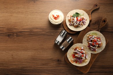 Delicious tacos with vegetables, meat and sauce on wooden table, flat lay. Space for text