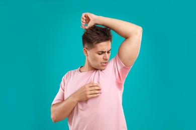 Young man with sweat stain on his clothes against blue background. Using deodorant