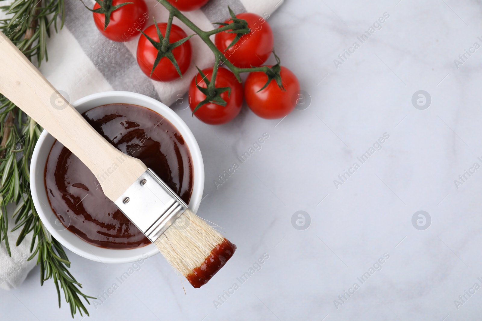 Photo of Marinade in bowl, basting brush, tomatoes and rosemary on white marble table, flat lay. Space for text