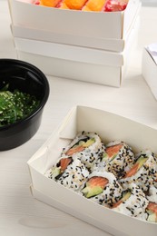 Food delivery. Paper boxes with delicious sushi rolls on white wooden table