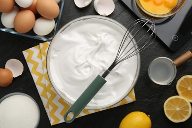 Bowl with whipped cream, whisk and ingredients on black table, flat lay