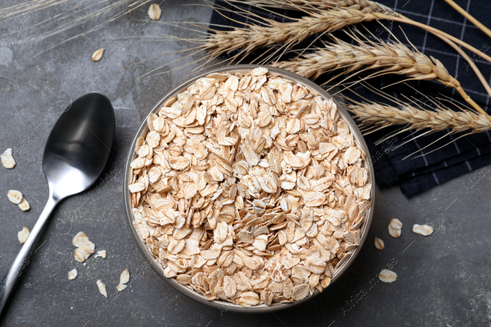 Photo of Bowl of oatmeal, spoon and spikelets on grey table, flat lay