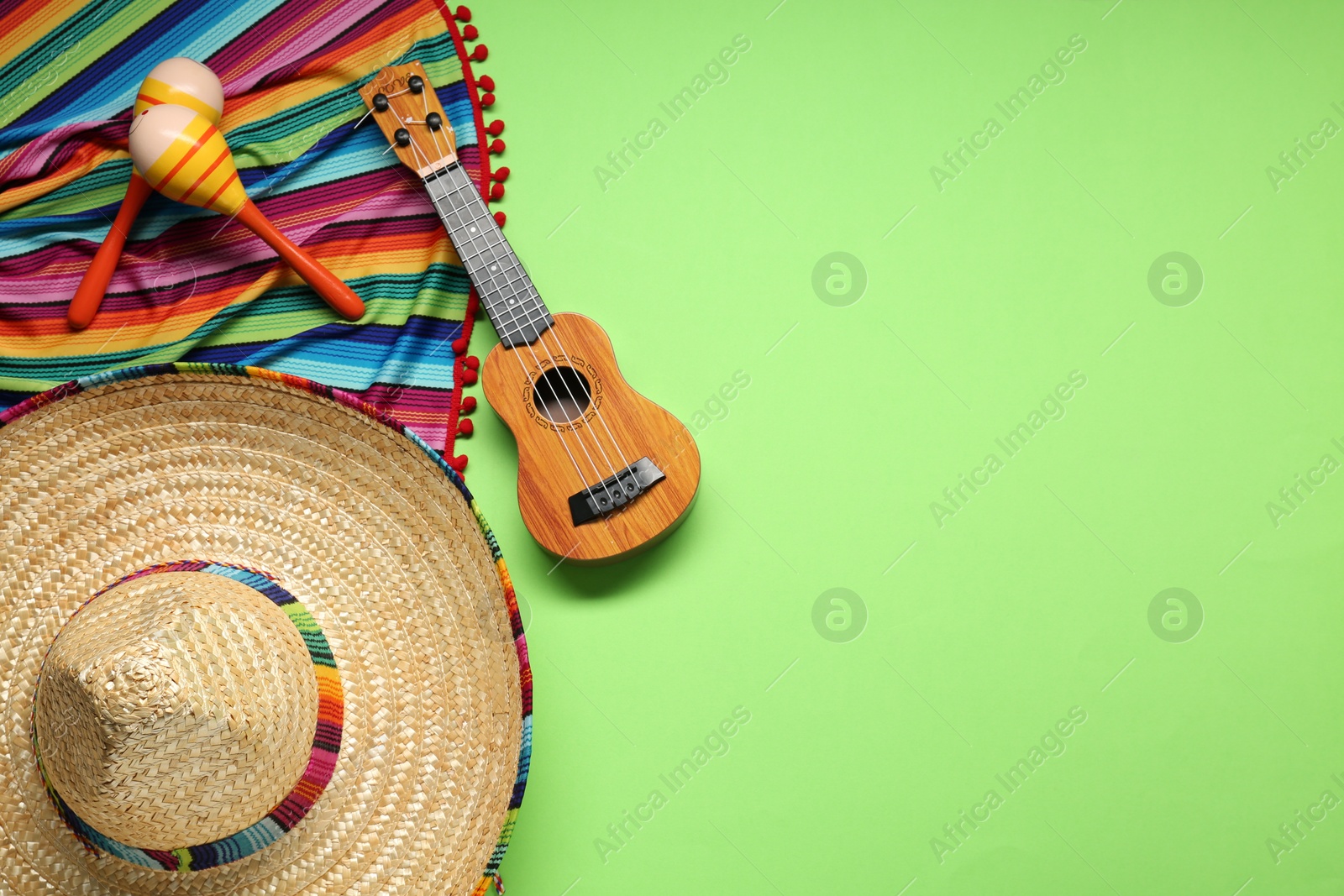 Photo of Mexican sombrero hat, guitar, maracas and colorful poncho on green background, flat lay. Space for text