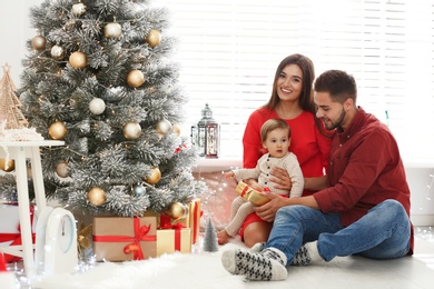 Happy family with cute baby near Christmas tree at home