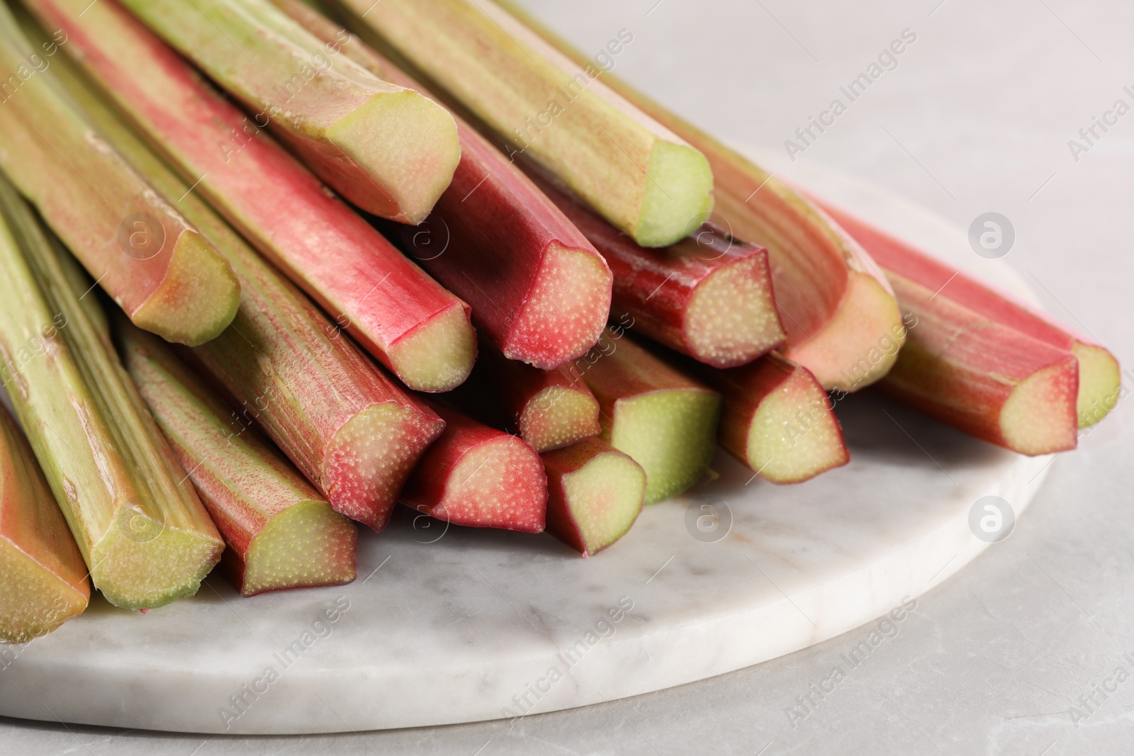 Photo of Fresh ripe rhubarb stalks on light grey table, closeup