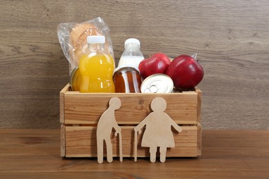 Humanitarian aid for elderly people. Different donation food products and figures of senior couple on wooden table