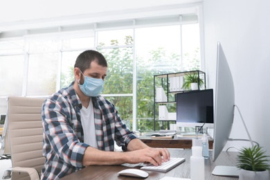 Photo of Office employee in respiratory mask at workplace