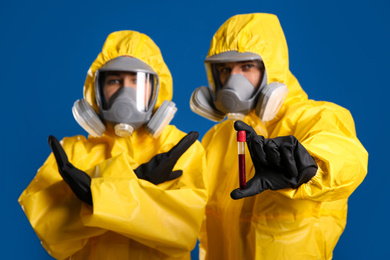 Man and woman in chemical protective suits with test tube of blood sample against blue background. Virus research
