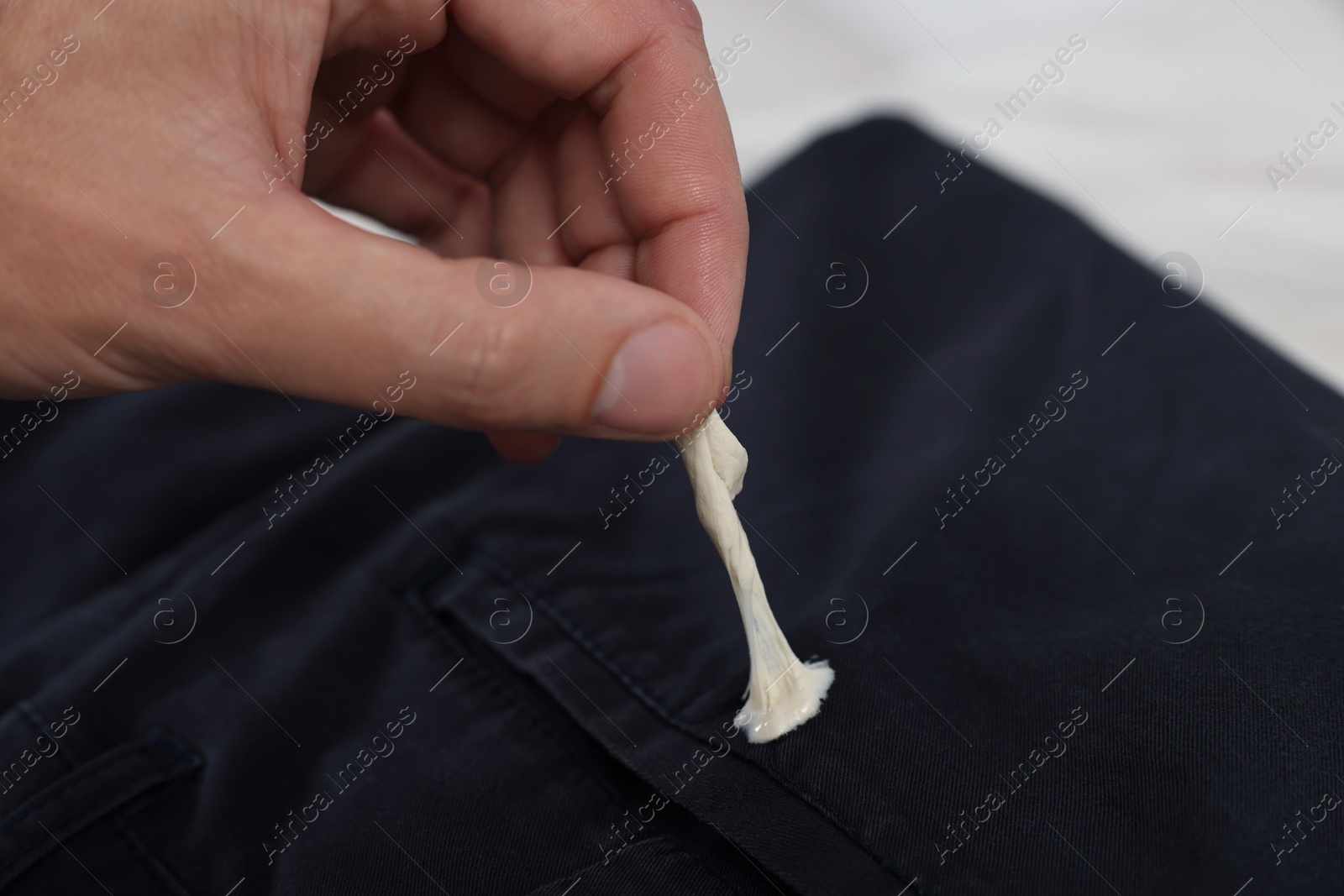 Photo of Man removing chewing gum from black jeans on white background, closeup