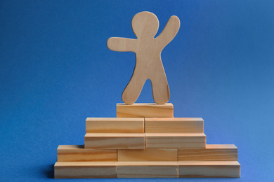 Photo of Wooden human figure on top of pyramid against blue background. Career promotion concept