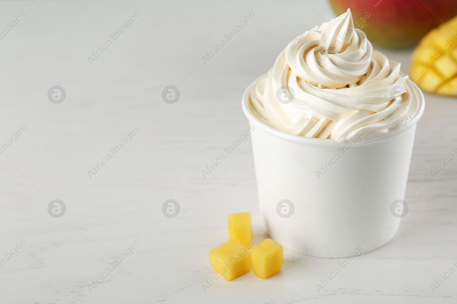 Photo of Cup with tasty frozen yogurt and mango on light wooden table. Space for text