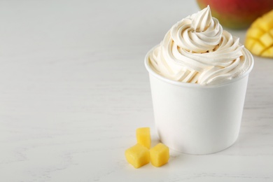 Cup with tasty frozen yogurt and mango on light wooden table. Space for text