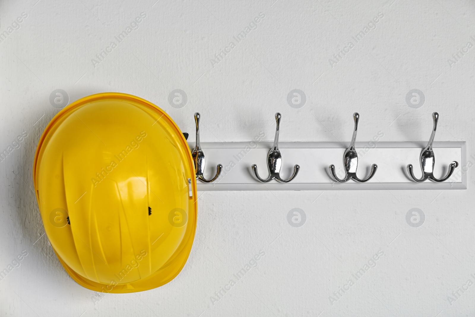 Photo of Hard hat hanging on white wall. Safety equipment