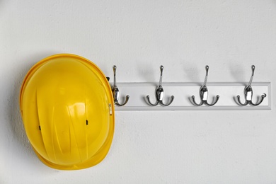 Photo of Hard hat hanging on white wall. Safety equipment