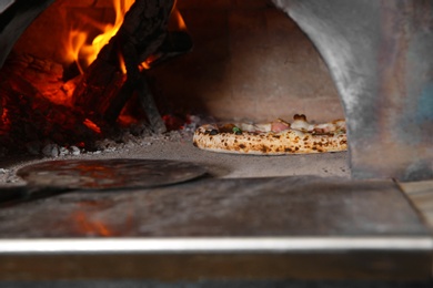 Photo of Burning firewood and tasty pizza in oven at restaurant kitchen
