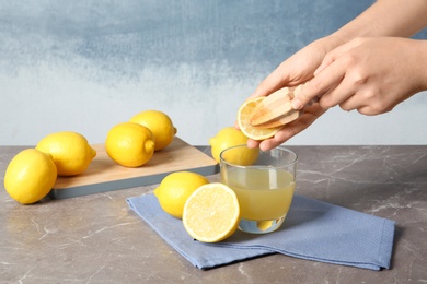 Woman squeezing lemon juice with reamer into glass on table