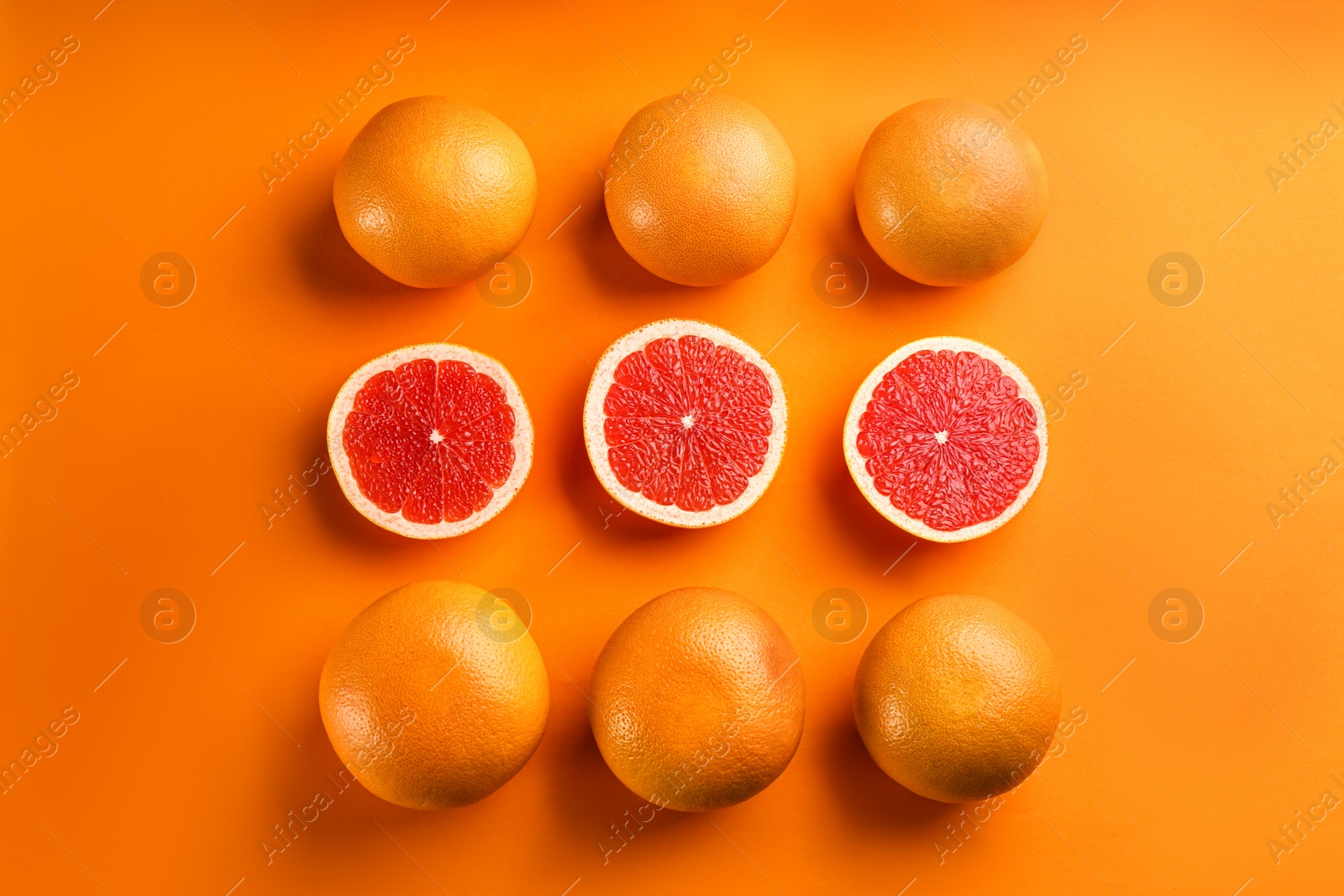 Photo of Cut and whole ripe grapefruits on orange background, flat lay