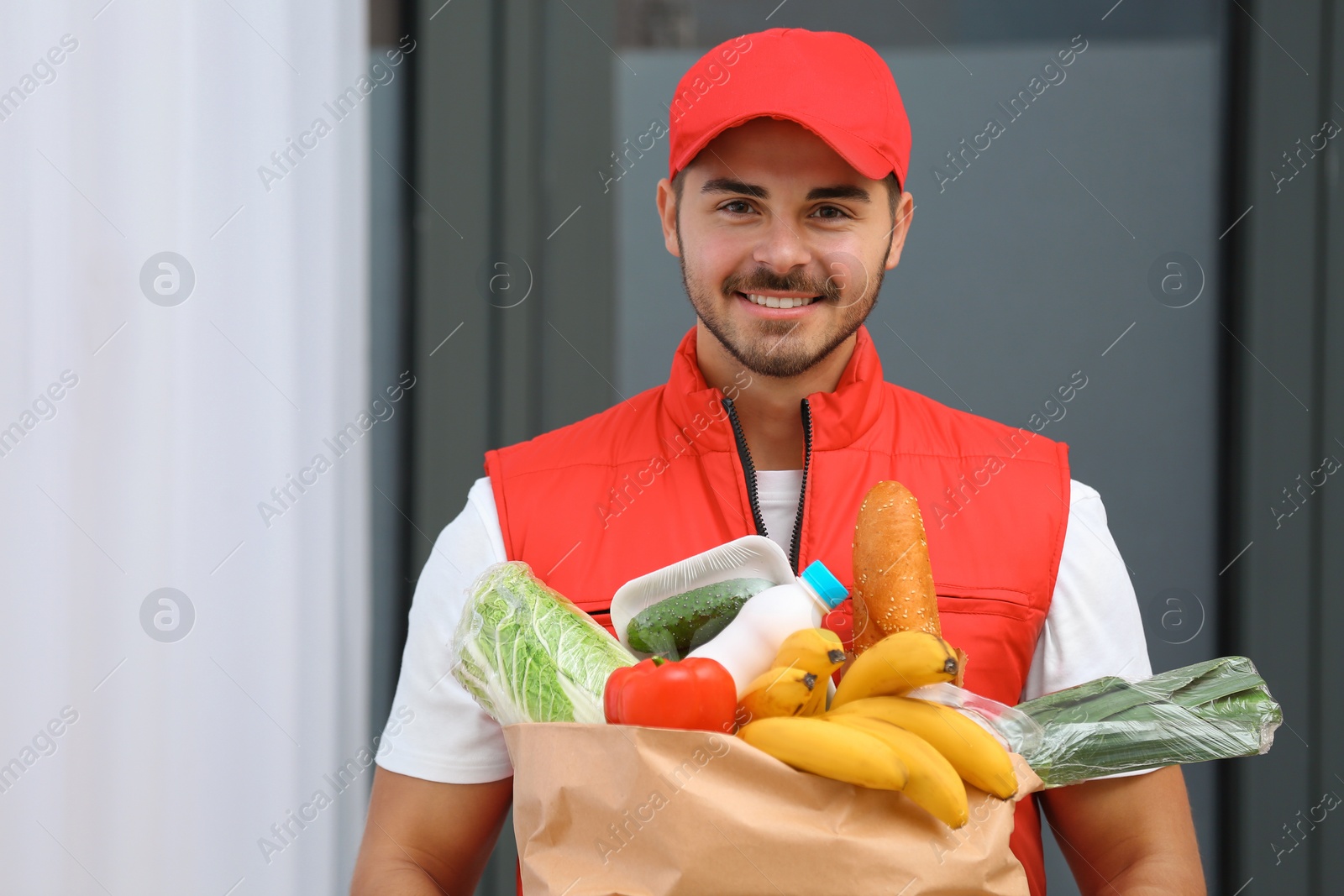 Photo of Male courier holding paper bag with products indoors. Food delivery service