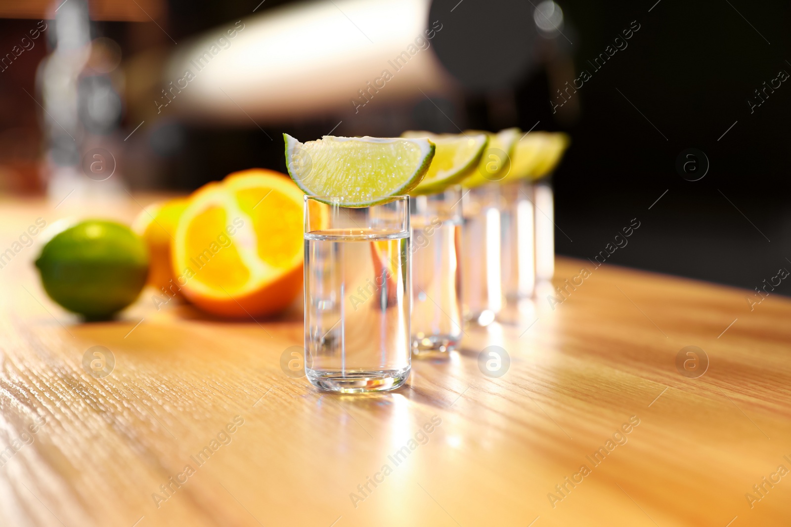 Photo of Vodka shots and lime slices on wooden bar counter