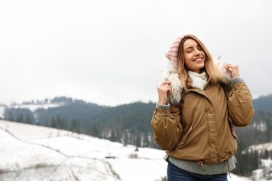 Photo of Young woman in warm clothes near snowy hill, space for text. Winter vacation