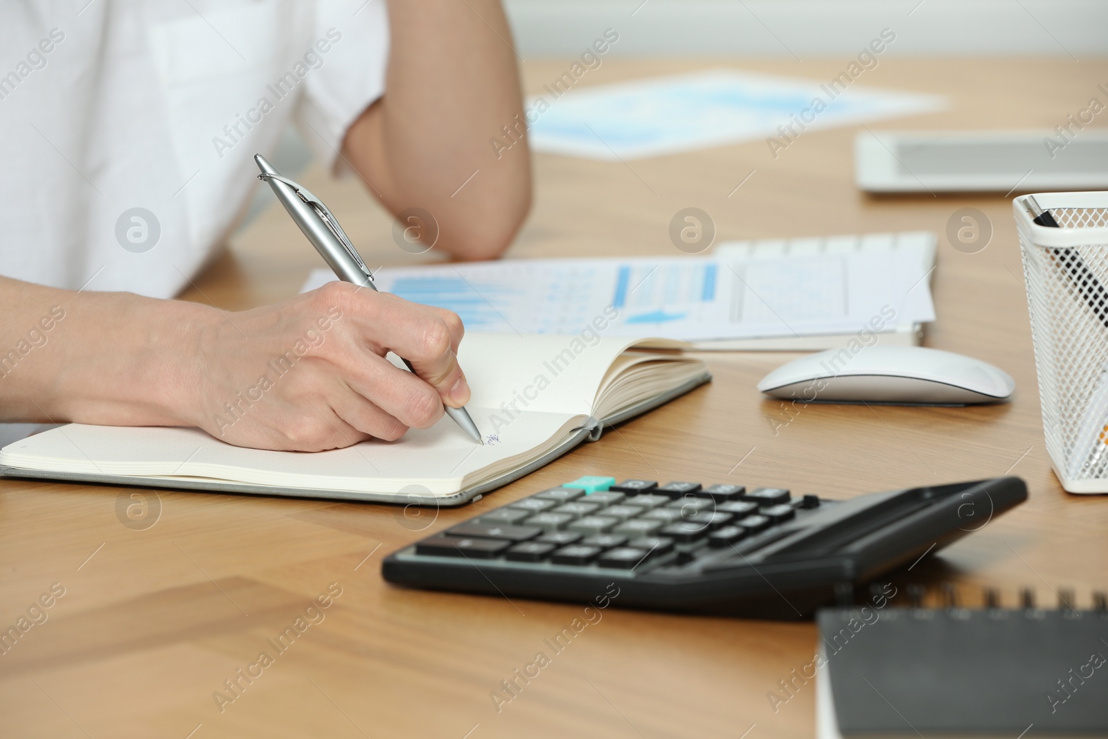 Photo of Professional accountant writing in notebook at wooden desk in office, closeup