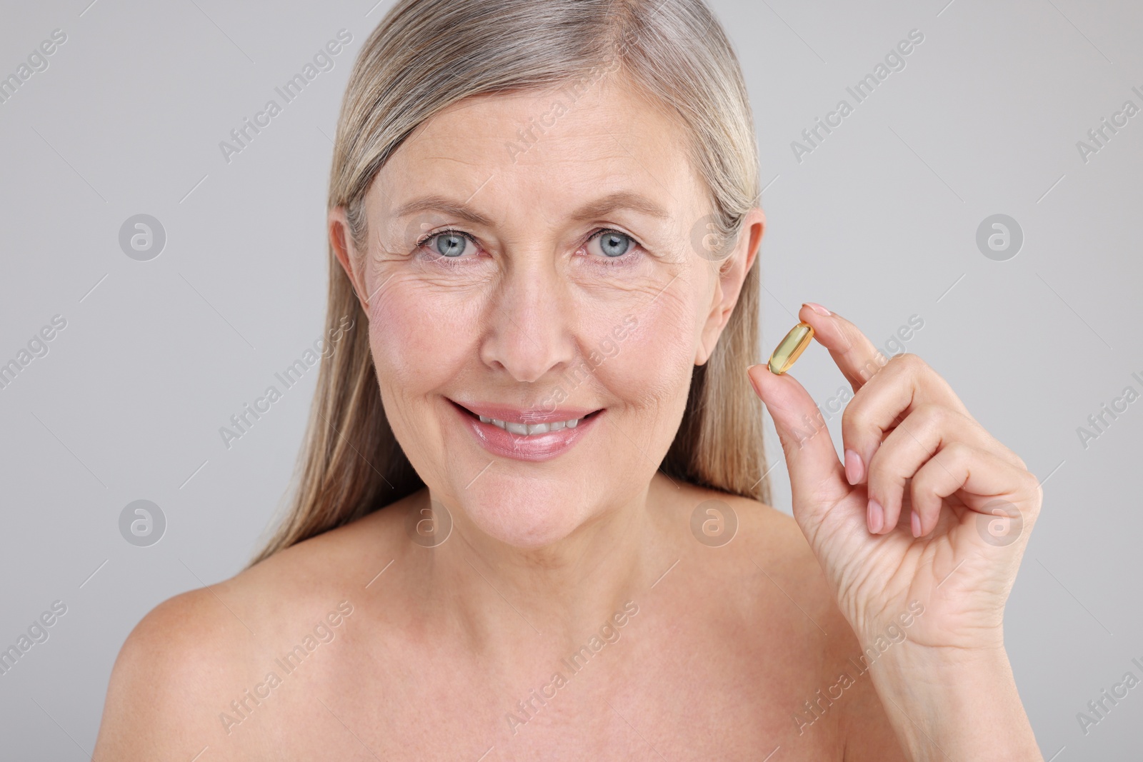 Photo of Beautiful woman with vitamin capsule on grey background