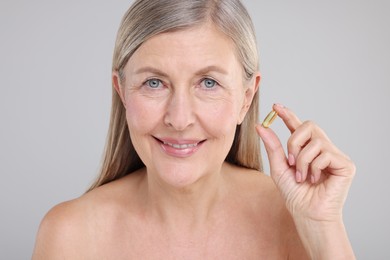 Beautiful woman with vitamin capsule on grey background