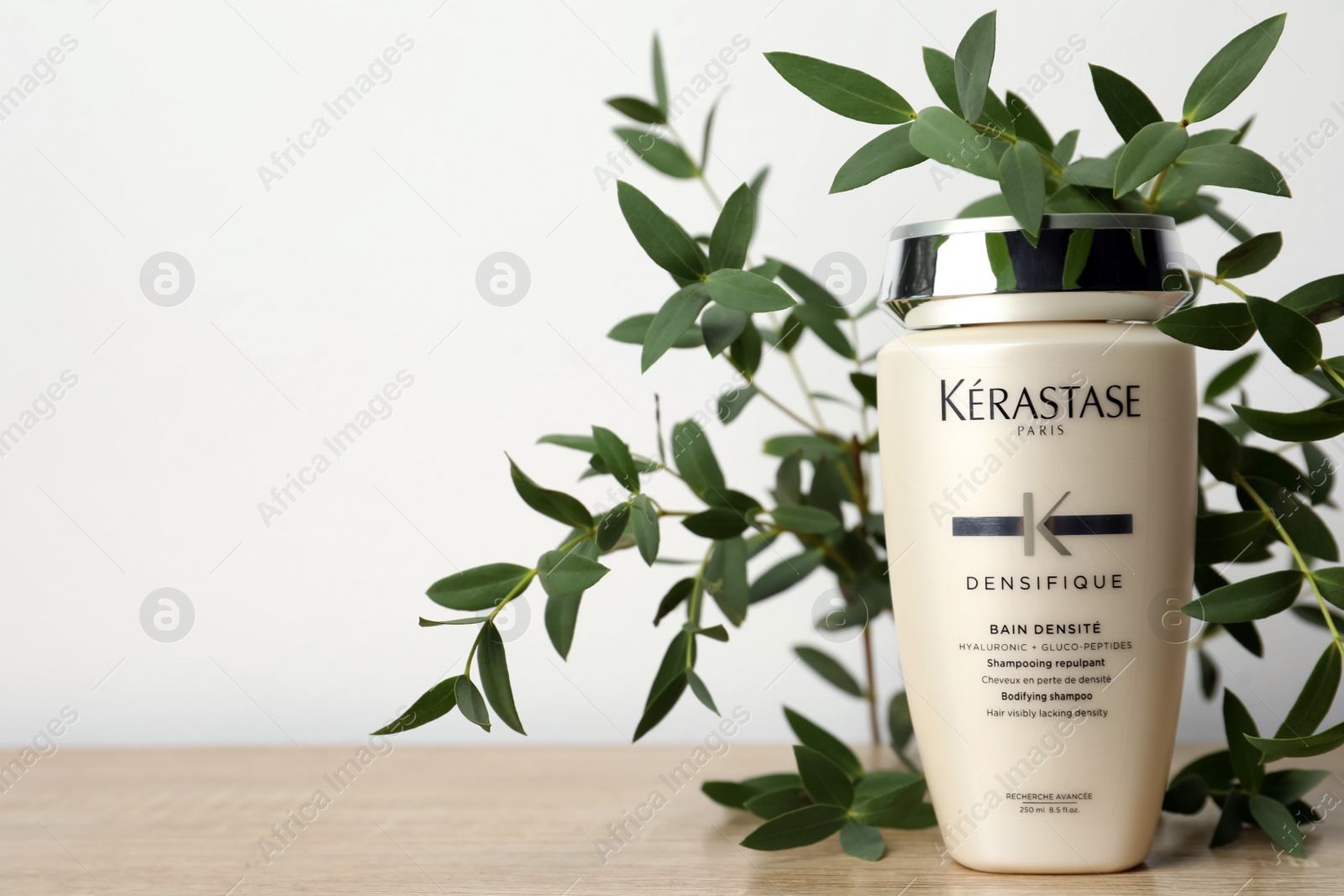 Photo of MYKOLAIV, UKRAINE - SEPTEMBER 07, 2021: Kerastase shampoo and green branches on wooden table. Space for text