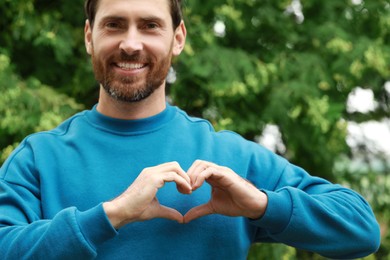 Photo of Happy man making heart with hands outdoors, closeup