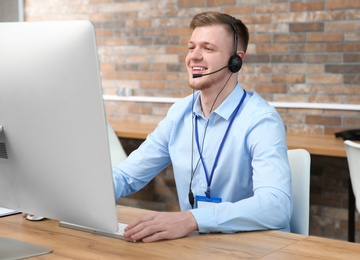 Photo of Technical support operator working with headset and computer at table in office