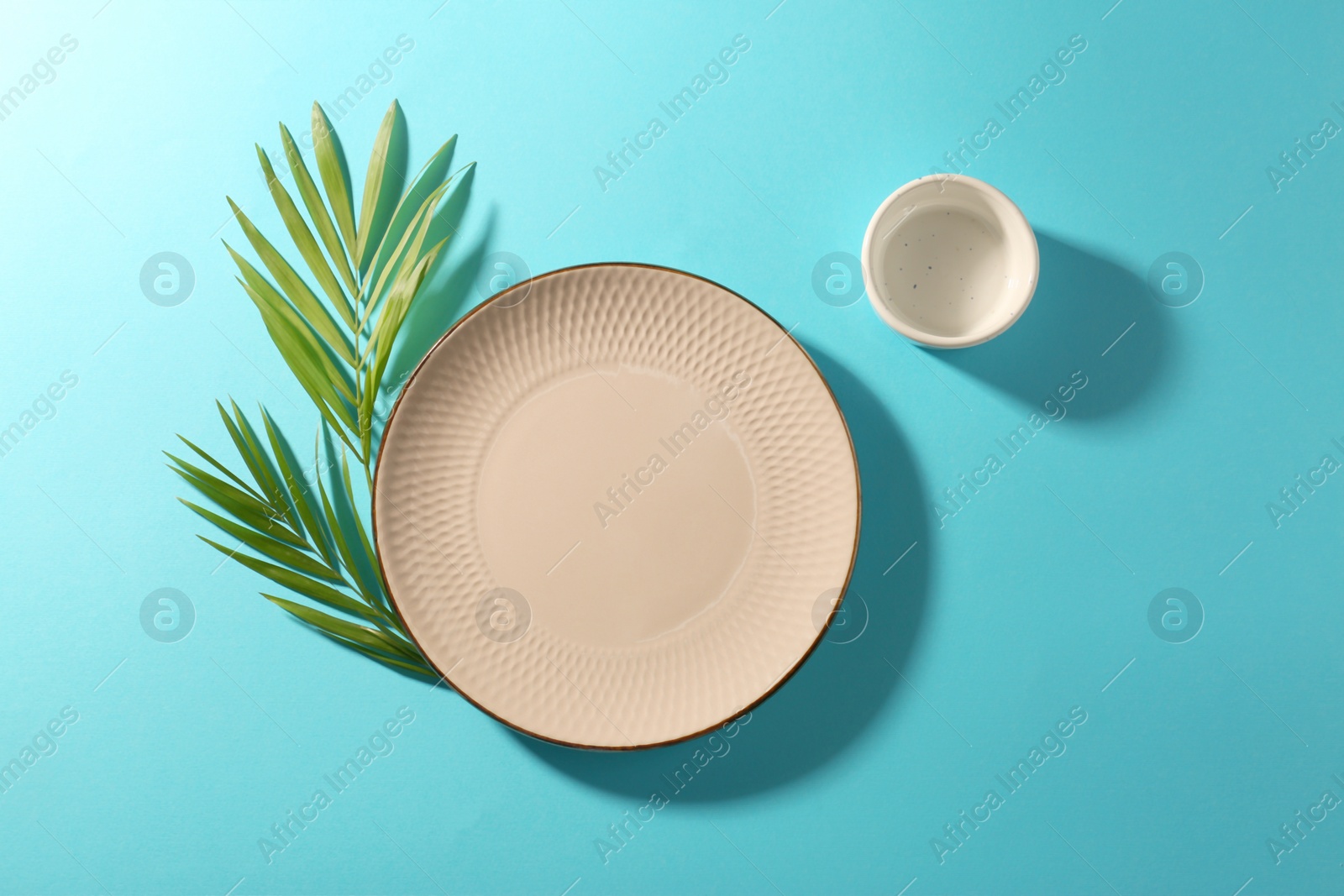 Photo of Ceramic plate, bowl and green leaves on turquoise background, flat lay